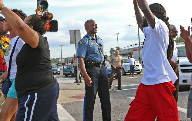 Capt. Ronald Johnson of the Missouri Highway Patrol smiles at demonstrators march along West Florissant Avenue in Ferguson, Mo., on Thursday, Aug. 14, 2014. The Missouri Highway Patrol took control of a St. Louis suburb Thursday, stripping local police of their law-enforcement authority after four days of clashes between officers in riot gear and furious crowds protesting the death of an unarmed black teen shot by an officer.
