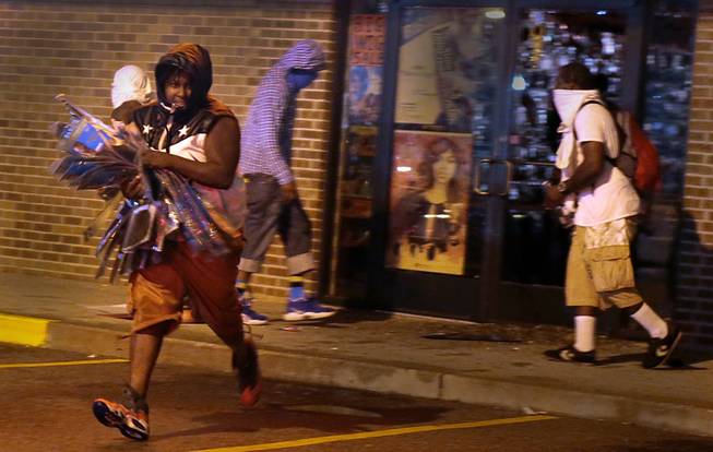 A looter escapes with items from Feel Beauty Supply on West Florissant Avenue in Ferguson early Saturday, Aug. 16, 2014, after protestors clashed with police.