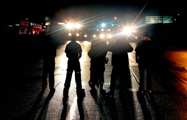 Against a backdrop of flood lights from police tactical vehicles, protestors stand their ground in the middle of West Florissant Avenue in Ferguson, refusing to leave despite police orders early Saturday, Aug. 16, 2014.