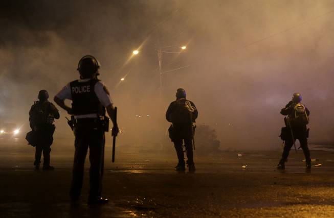 A law enforcement officer watches Sunday, Aug. 17, 2014, as tear gas is fired to disperse a crowd protesting the shooting of teenager Michael Brown last Saturday in Ferguson, Mo. Brown's shooting in the middle of a street following a suspected robbery of a box of cigars from a nearby market has sparked a week of protests, riots and looting in the St. Louis suburb. (AP Photo/)
