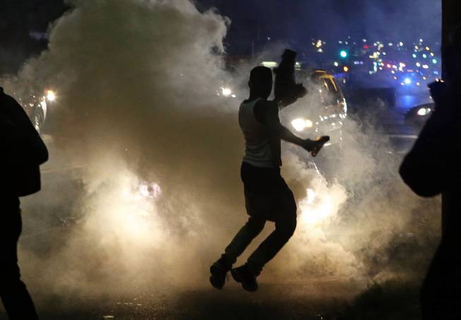 Protesters run when the police shoot tear gas in Ferguson, Mo., Sunday, Aug. 17, 2014. Protests over the killing of 18-year-old Michael Brown by a white police officer have entered their second week. 