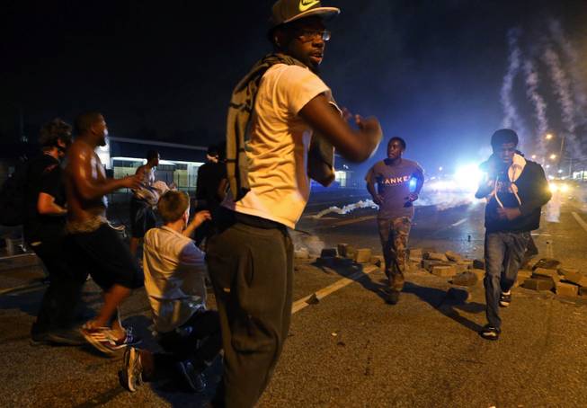 Protesters run when the police fire multiple tear gas canisters in Ferguson, Mo., Sunday, Aug. 17, 2014. Protests over the killing of 18-year-old Michael Brown by a white police officer have entered their second week. 