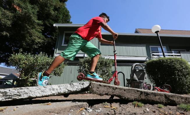 A youngster rides his scooter over a sidewalk buckled by an earthquake Sunday, Aug. 24, 2014, in Napa, Calif. A large earthquake caused significant damage and left at least three critically injured in California's northern Bay Area early Sunday, igniting fires, sending at least 87 people to a hospital, knocking out power to tens of thousands and sending residents running out of their homes in the darkness.