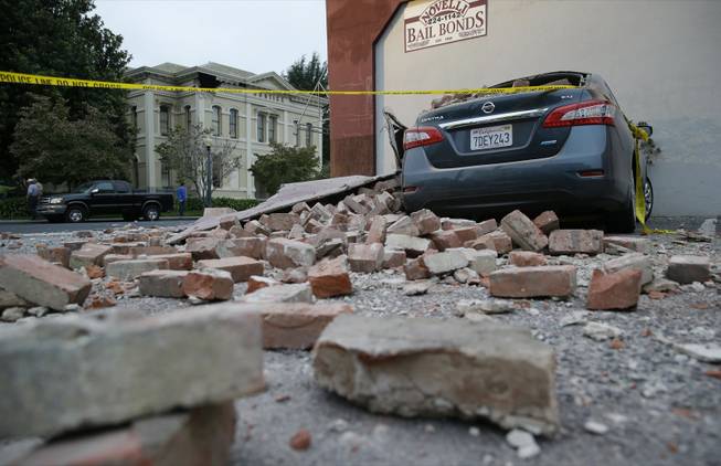 Bricks and fallen rubble cover a car with the old courthouse in the background after an earthquake Sunday, Aug. 24, 2014, in Napa, Calif. A large earthquake rolled through California's northern Bay Area early Sunday, damaging buildings, igniting fires, knocking out power to tens of thousands and sending residents running from their homes in the darkness.