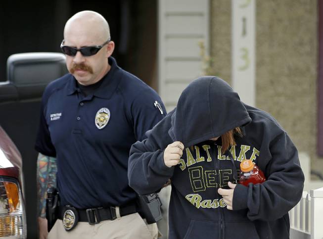 An unidentified woman is escorted from a home by a police officer after a baby was found in a garbage can in Kearns, Utah, on Tuesday, Aug. 26, 2014. 