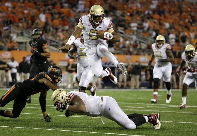 Florida State quarterback Jameis Winston leaps over guard Josue Matias as Oklahoma State safety Jordan Sterns, left, is unable to stop Winston from reaching the end zone for a touchdown in the second half of an NCAA football game Saturday, Aug. 30, 2014, in Arlington, Texas.