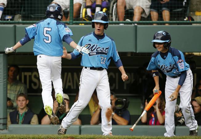 Las Vegas' Justin Hausner leaps on home plate and celebrates with teammates Austin Kryszczuk, center, and Brad Stone after all three scored on a double by Drew Laspaluto off Chicago's Joshua Houston in the first inning of the U.S. championship game at the Little League World Series tournament in South Williamsport, Pa., Saturday, Aug. 23, 2014.