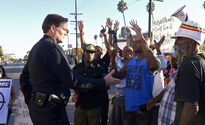 Protesters hold their hands up as a Los Angeles Police Department officer tries to talk to them in front of the 77th Street police station in Los Angeles during a protest of the LAPD shooting of Ezell Ford. Police say that Ford had attempted to remove a gun from an officer's holster on Monday when he was shot and killed, which differs from accounts by the family of the man.