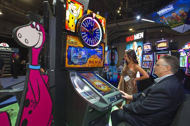 Michael Moosman of Bally Technologies tries out a Flintstones-themed slot machine in the WMS Gaming booth as "cavewoman" Ayla Brown looks on during the final day of the Global Gaming Expo (G2E) at the Sands Expo Center Thursday, Oct. 2, 2014.