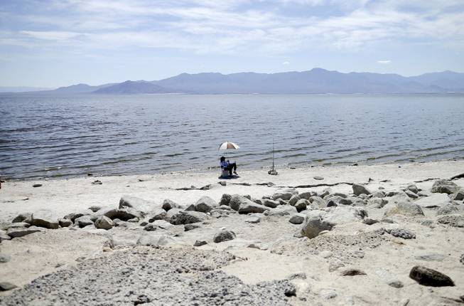 In this April 30, 2015, photo, Ed Victoria of Los Angeles sits under an umbrella as he fishes for tilapia along the receding banks of the Salton Sea near Bombay Beach, Calif. The lake is shrinking and on the verge of getting smaller as more water goes to coastal cities. 