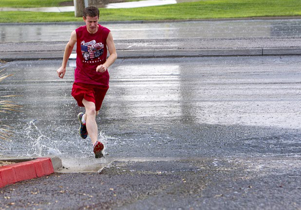 A pedestrian jumps over flood runoff as he crosses Sunset Road during a thunderstorm in Henderson, Aug. 13, 2015.