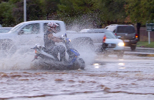 A scooter driver goes through flood waters at there intersection of Sunset Road and Whitney Ranch Drive during a thunderstorm in Henderson, Aug. 13, 2015.