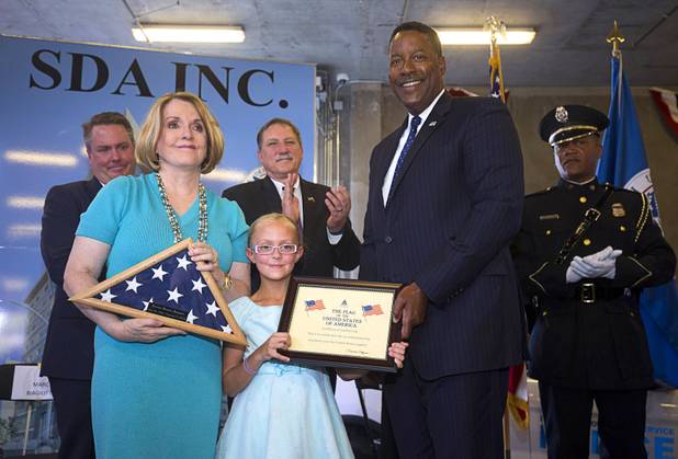 Paula Biagiotti and her granddaughter Sydney, 8, pose with a flag presented by Peter Edge, right, executive associate director for Homeland Security Investigations, during an opening ceremony for the Federal Justice Tower, a new office building in downtown Las Vegas, Thursday, Aug. 18, 2016. Paula Biagiotti is the widow of developer Stephen Biagiotti, founder of SDA Inc., which built the building.