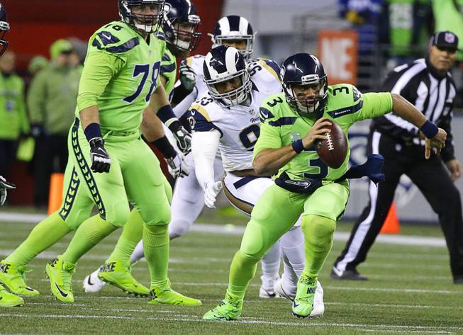 Seattle Seahawks quarterback Russell Wilson (3) scrambles away from Los Angeles Rams defensive end Ethan Westbrooks, center, in the first half of an NFL football game, Thursday, Dec. 15, 2016, in Seattle. 