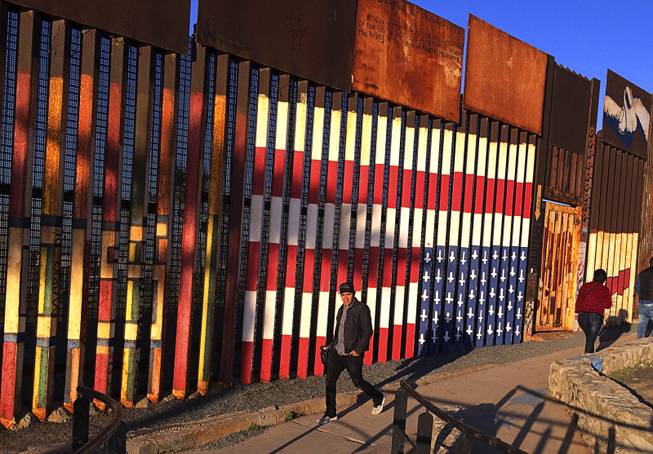 People pass graffiti along the border structure in Tijuana, Mexico, Wednesday, Jan. 25, 2017. President Donald Trump moved aggressively to tighten the nation's immigration controls Wednesday, signing executive actions to jumpstart construction of his promised U.S.-Mexico border wall and cut federal grants for immigrant-protecting "sanctuary cities." 