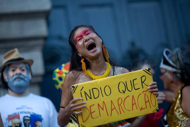 A reveler holds a sign Friday, Feb. 24, 2017, that reads in Portuguese, "Indians want demarcation," during the "Out Temer" carnival street party in Rio de Janeiro, Brazil. Merrymakers took to the streets to protest Brazil's President Michel Temer.