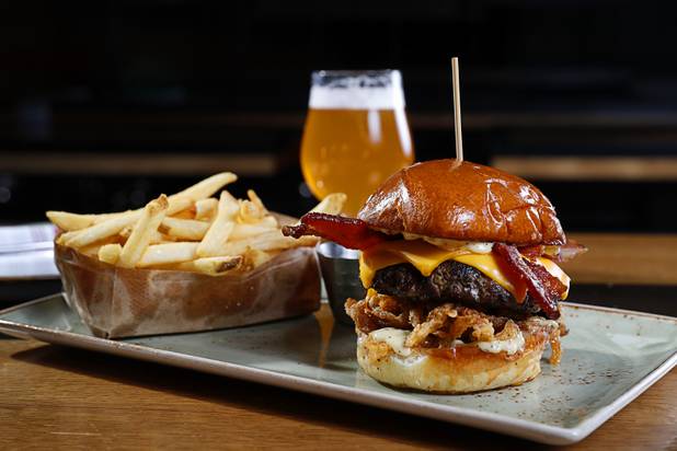 The White Truffle Bacon Aioli Burger at Public School 702 in Downtown Summerlin Monday, April 17, 2017. The bacon and cheese burger with a white truffle and cherry vinaigrette aioli is served on crispy onion straws. Paired with your choice of three beers, the burger and fries combo is $13.00 through April.