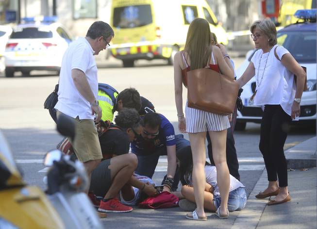 An injured person is treated in Barcelona, Spain, Thursday, Aug. 17, 2017, after a white van jumped the sidewalk in the historic Las Ramblas district, crashing into a summer crowd of residents and tourists.