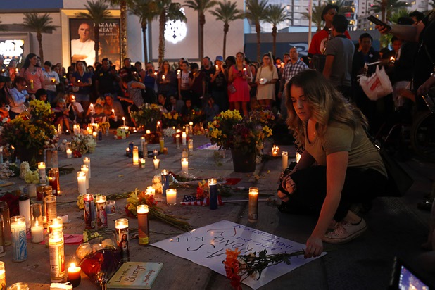 A woman places a sign and flowers at a makeshift memorial during a vigil, marking the one-week anniversary of the Oct. 1 mass shooting, at Sahara Avenue and The Strip Sunday, Oct. 8, 2017.