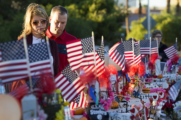 A couple looks over look over 58 wood crosses, with the names and photos of the Oct. 1 mass shooting victims, in the median of Las Vegas Boulevard South near the "Welcome to Las Vegas" sign Monday, Oct. 9, 2017.