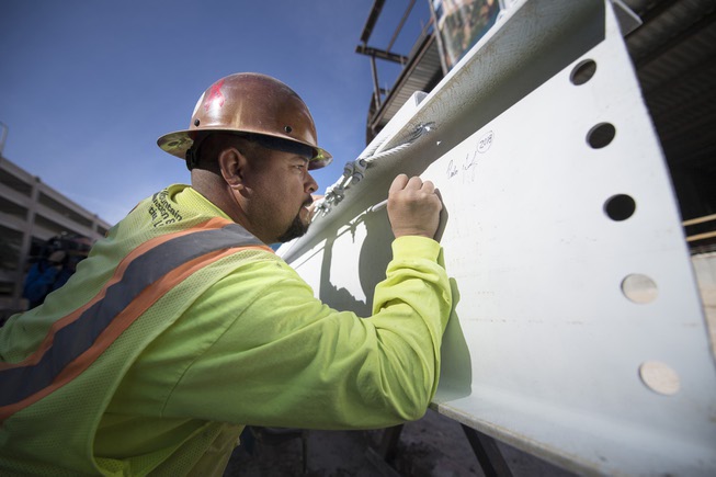 An iron worker signs the final steel beam that will ...