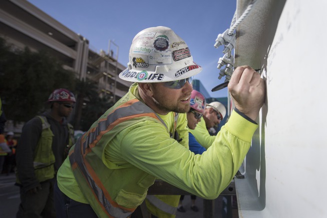 An iron worker signs the final steel beam that will ...