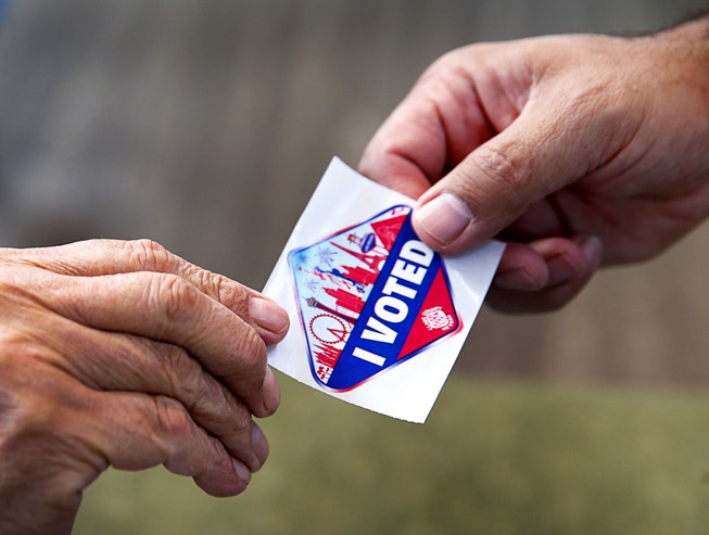 An election worker hands a sticker to a voter during ...