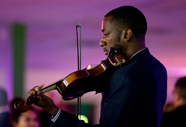 A strolling violinist entertains guests during the grand opening of Oasis Biotech, an indoor microgreen and herb vertical farming facility, Wednesday, July 18, 2018.