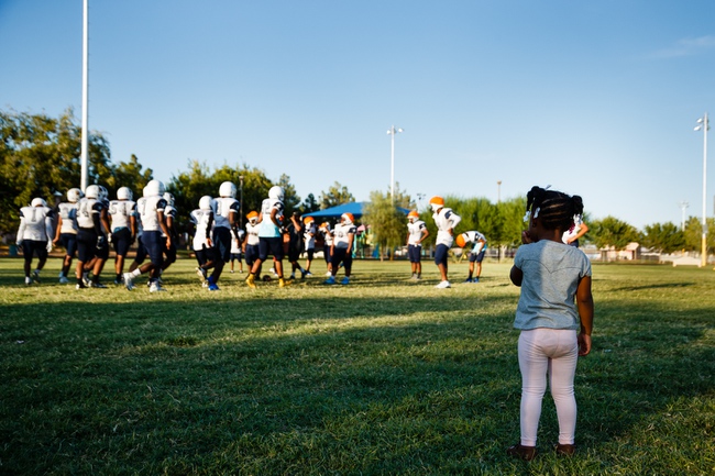 A little girl watches football players from Democracy Prep Academy practice at Kianga Isoke Palacio Park, Tuesday, Aug. 28, 2018. Practice is conducted at the nearby park because the school doesn't have its own field.