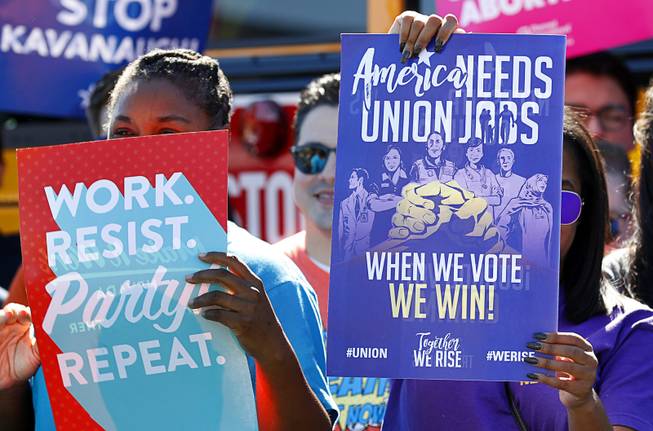 ShaRonda Ramos, left, representing Make It Work Nevada, and Regina Toney, a communications specialist with the SEIU Union, hold up signs during a "Hop on the Progress Bus" news conference in an office park parking lot on West Sahara Avenue Wednesday, Sept. 19, 2018.