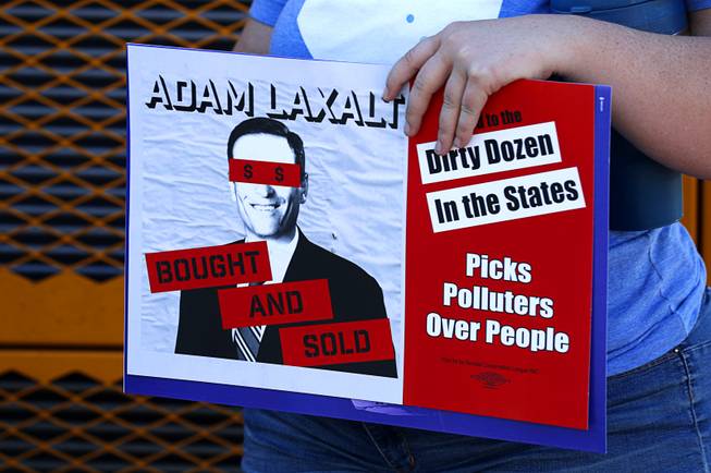 A woman holds a sign with an image of Nevada Attorney General Adam Laxalt, the Republican candidate for Nevada governor, during a "Hop on the Progress Bus" news conference in an office park parking lot on West Sahara Avenue Wednesday, Sept. 19, 2018. A coalition of progressive groups joined to hold the news conference a day before President Trump's visit to Las Vegas.