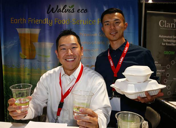 Jason Ra, president of Walvis Eco Foodservice Products, and Daisuke Graupp, pose with biodegradable cups and clamshell boxes during the Nightclub & Bar Convention and Trade Show at the Las Vegas Convention Center Tuesday, March 26, 2019. The cups are make of corn starch and the boxes as made from the stalks of sugar cane.