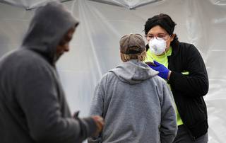 A woman gets information from a homeless man as a temporary homeless shelter overflow facility opens at a Cashman Center parking lot Saturday, March 28, 2020. Officials established the camp to house residents who were displaced when Catholic Charities closed due to coronavirus concerns.