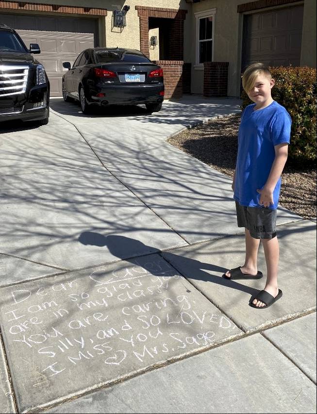 Caden Collier poses for a photo next to a message written on his driveway by his Pinecrest Academy teacher Avery Sage. 