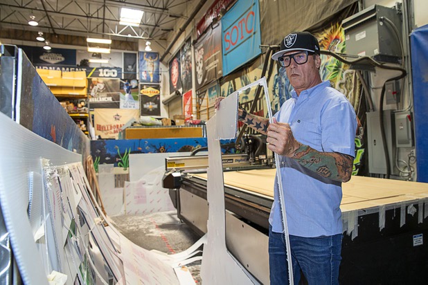 Owner James Swanson holds a protective polycarbonate barrier near a computer-controlled router table at Screaming Images Thursday, May 7, 2020. Screaming Images is a graphic design and installation firm.