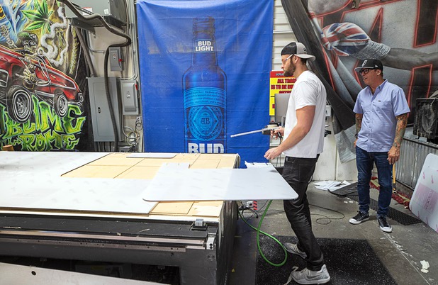 Sean Southam makes protective polycarbonate barrier at Screaming Images Thursday, May 7, 2020. Owner James Swanson looks on at right. The barriers have a variety of applications in gaming, business and office space.