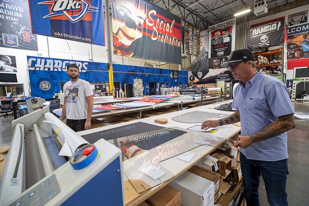 Sean Southam and owner James Swanson look over a protective polycarbonate barrier at Screaming Images Thursday, May 7, 2020. The barriers have a variety of applications in gaming, business and office space.