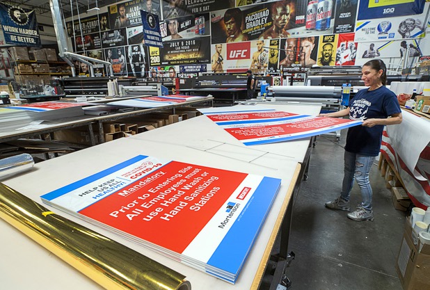 Quality control inspector Lilly Hernandez looks over COVID 19-related signage at Screaming Images Thursday, May 7, 2020. Screaming Images is a graphic design and installation firm.