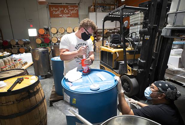 Distillery workers Will Wood, left, and Julian Morales pump glycerin from a barrel as they mix hand sanitizer at the Las Vegas Distillery in Henderson Wednesday, May 13, 2020. The distillery has switched from making distilled spirits to hand sanitizer in order to help in the fight against the novel coronavirus (COVID-19).