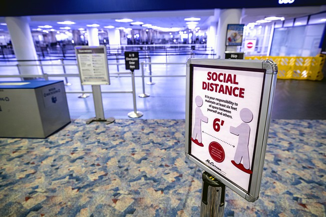 A sign reminds passengers of social distancing by a security ...