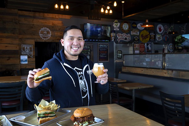 Van-Alan Nguyen, owner of 595 Craft and Kitchen and Art District Kitchen, poses with a Pork Belly Banh Mi and a glass of Beachwood Brewing's "Khakis & Car Keys?" IPA in 595 Craft at Rainbow Boulevard and Tropicana Avenue Wednesday, Nov. 11, 2020. Also pictured is a Nashville-style Hot Chicken Sandwich.