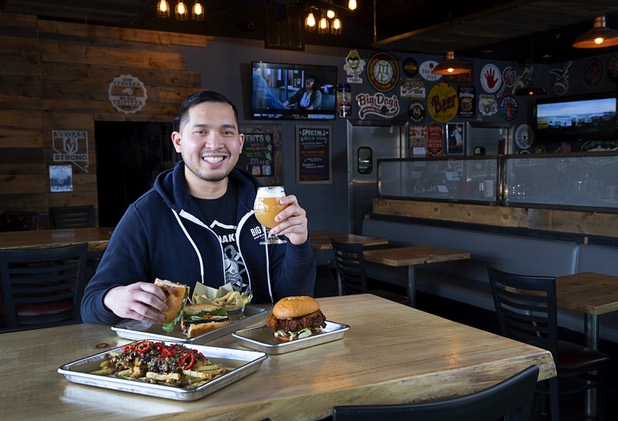 Van-Alan Nguyen, owner of 595 Craft and Kitchen and Art District Kitchen, poses with a Pork Belly Banh Mi and a glass of Beachwood Brewing's "Khakis & Car Keys?" IPA in 595 Craft at Rainbow Boulevard and Tropicana Avenue Wednesday, Nov. 11, 2020. Also pictured are Hangover Fries and a Nashville-style Hot Chicken Sandwich.