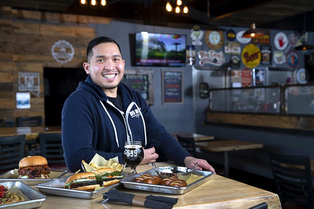 Van-Alan Nguyen, owner of 595 Craft and Kitchen and Art District Kitchen, poses in 595 Craft at Rainbow Boulevard and Tropicana Avenue Wednesday, Nov. 11, 2020. Dishes include a Nashville-style Hot Chicken Sandwich, left, a Pork Belly Banh Mi, center, and Beer Cheese with Soft Pretzels.