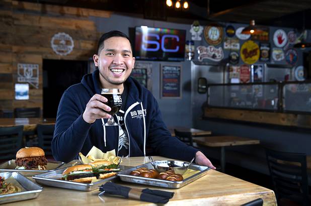 Van-Alan Nguyen, owner of 595 Craft and Kitchen and Art District Kitchen, poses in 595 Craft at Rainbow Boulevard and Tropicana Avenue Wednesday, Nov. 11, 2020. Dishes include a Nashville-style Hot Chicken Sandwich, left, a Pork Belly Banh Mi, center, and Beer Cheese with Soft Pretzels.