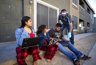 Joel Bradley, a student success advocate, shows seventh grader Andre Brown how to properly sign-in for his classes outside his apartment Wednesday, Nov. 18, 2020. Also pictured are Brown's cousin Jazmine Melendez, left, and his sister Aneessa.