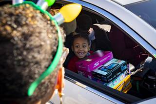 A child receives toys and shoes from a volunteer during a drive-thru charity event sponsored by local philanthropist Bob Ellis at Martinez Elementary School in North Las Vegas, Thursday, Dec. 17, 2020.