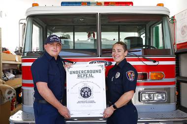Cody Milner, a firefighter at the Nevada National Security Site, and Amanda Snider, a Clark County firefighter, pose at the Firefighters of Southern Nevada Burn Foundation offices Tuesday, June 29, 2021, with a poster promoting the upcoming firefighter auction.