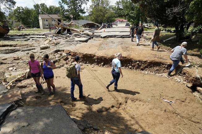People walk across a washed out road Sunday, Aug. 22, 2021, in Waverly, Tenn. Heavy rains caused flooding Saturday in Middle Tennessee and have resulted in multiple deaths and property destruction.

