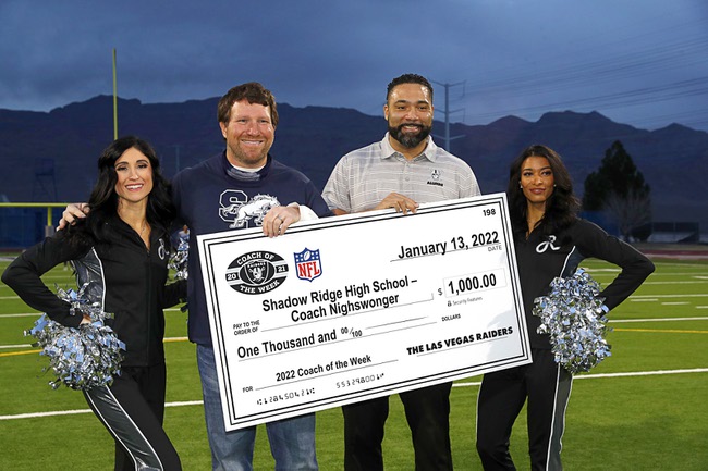 Raiderettes Nicola, left, and Monet join Raiders alumni Teyo Johnson as they present an oversized check to Shadow Ridge coach Matt Nighswonger before a flag football game between the Shadow Ridge Mustangs and the Bonanza Bengals at Shadow Ridge High School Thursday, Jan. 13, 2022.