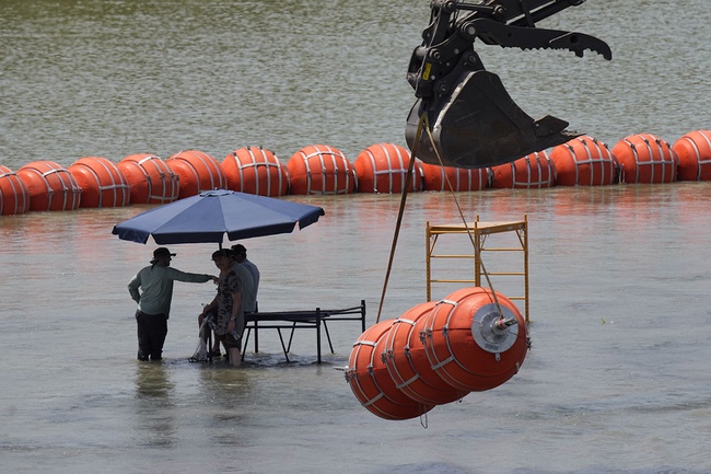 Workers take a break from deploying large buoys to be used as a border barrier along the banks of the Rio Grande in Eagle Pass, Texas, Wednesday, July 12, 2023. The floating barrier is being deployed in an effort to block migrants from entering Texas from Mexico.